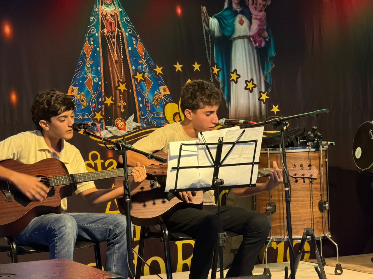 Alunos se apresentam com violões e microfones no palco da festa